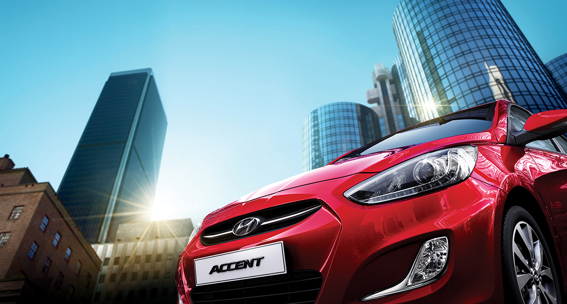 منظر سفلي للجانب الأمامي لسيارة أكسنت الحمراء مع أبراج المدينة في الخلفية