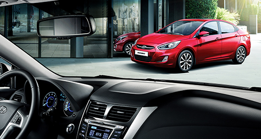 منظر أمامي جانبي لسيارة أكسنت الحمراء متوقفة أمام مبنى من زاوية نظر الراكب عبر الزجاج الأمامي