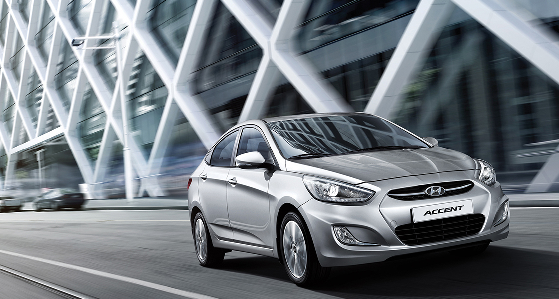 منظر أمامي جانبي لسيارة أكسنت الفضية تمر بجانب مبنى بحائط مزخرف