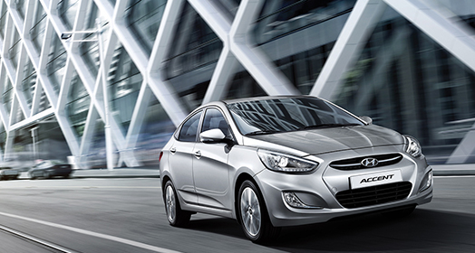 منظر أمامي جانبي لسيارة أكسنت الفضية تمر بجانب مبنى بحائط مزخرف