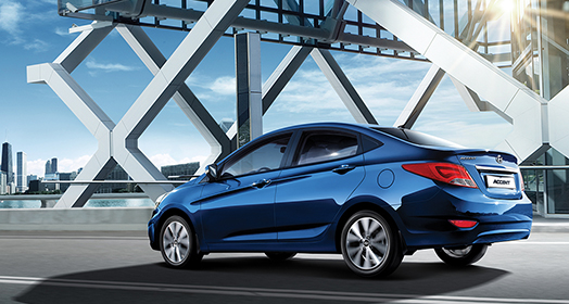 منظر جانبي لسيارة أكسنت الزرقاء أثناء قيادتها على الطريق مع آشعة الشمس في الخلفية