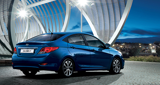 منظر خلفي جانبي لسيارة أكسنت الزرقاء متوقفة أمام الهيكل المعماري على شكل قوس في المساء