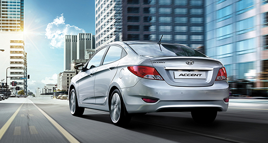 منظر خلفي جانبي لسيارة أكسنت الفضية أثناء قيادتها عبر أبراج المدينة