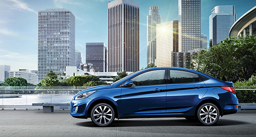 منظر جانبي لسيارة أكسنت الزرقاء أثناء قيادتها على الطريق مع مشهد لأفق المدينة في الخلف