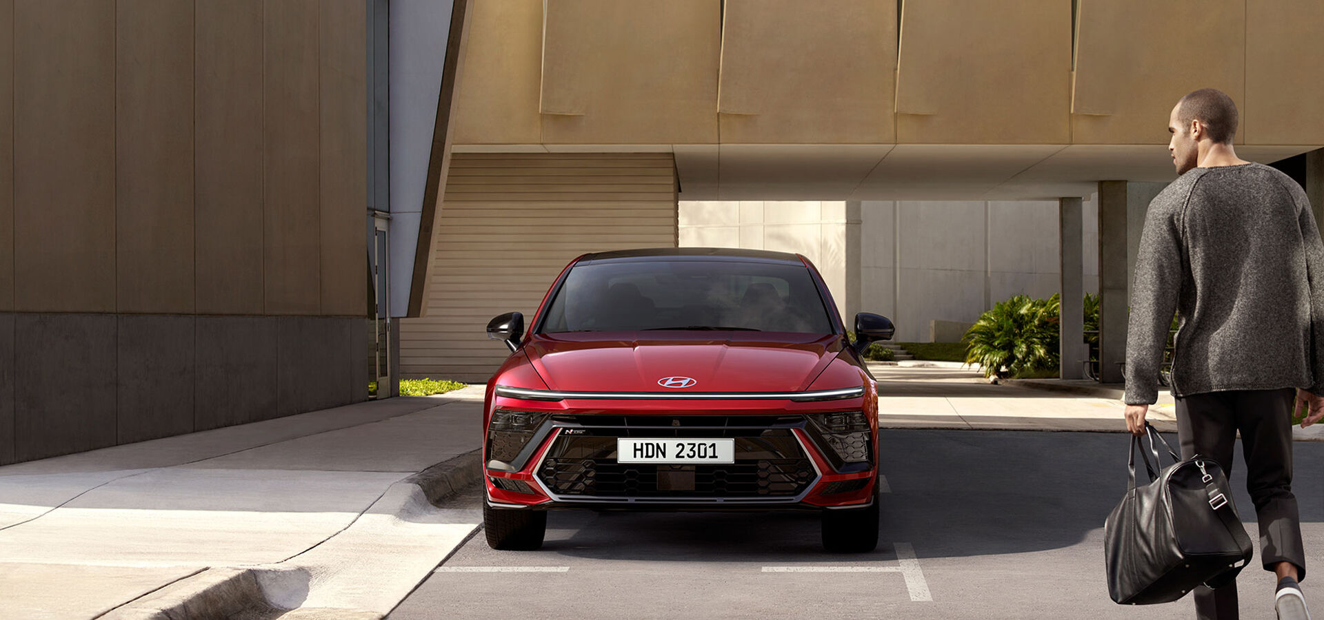 A scene in which the front view of a red SONATA N Line is seen standing in a parking space, and the back of a man dressed in gray approaches the car from the right side of the screen.