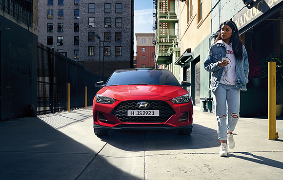 A woman and front view of red veloster parking on the road 