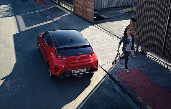 A woman and left side rear view of red veloster parking on the road 