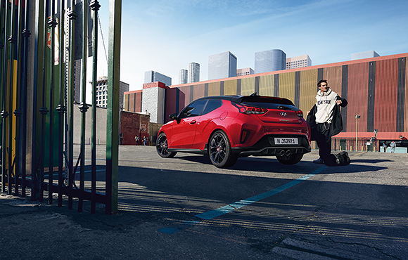 A man and left side rear view of red veloster parking on the road