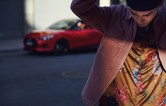 Red veloster parking on the road behind a man.