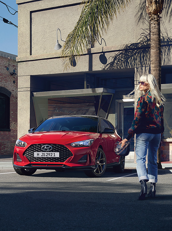 Red Veloster parked on the road beside blond woman